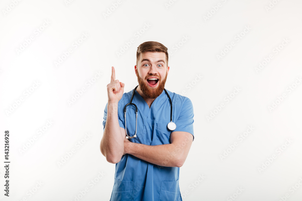 Excited young male doctor pointing finger up at copyspace Excited young male doctor pointing finger up at copyspace
