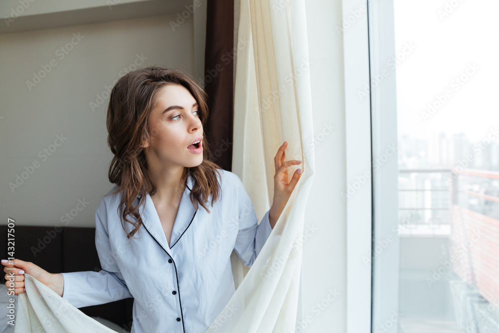 Young woman opens curtains to look at the view Young woman opens curtains to look at the view
