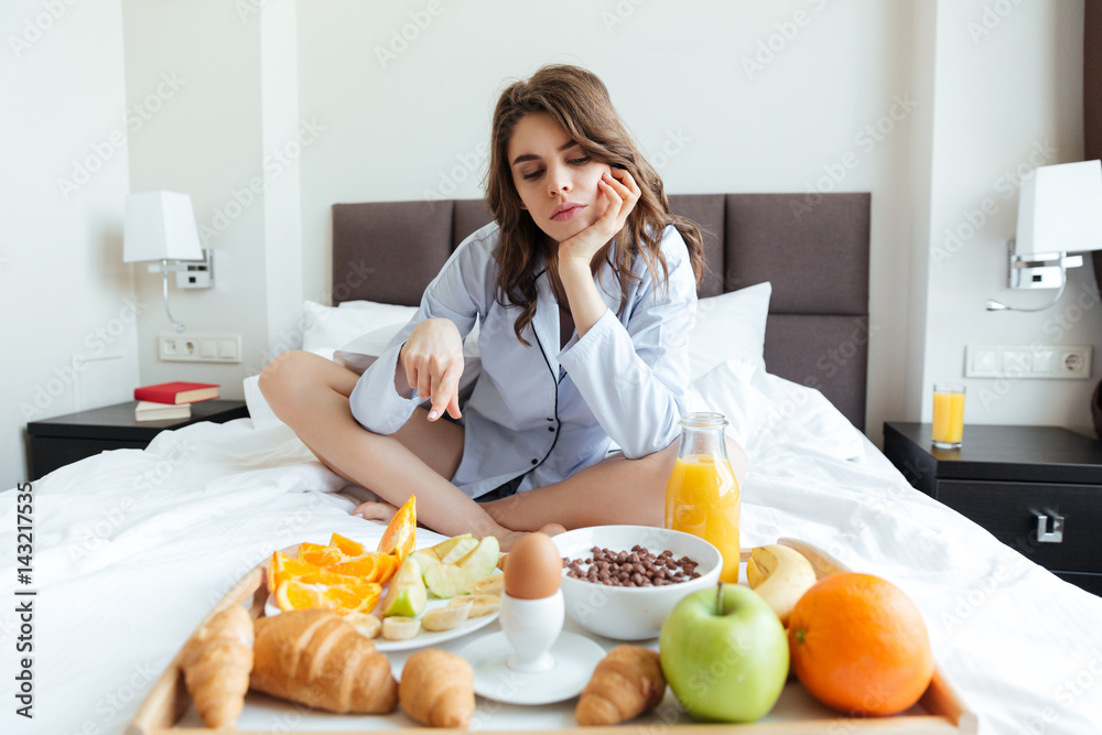 Woman sitting on bed and pointing at tray with breakfast Woman sitting on bed and pointing at tray with breakfast