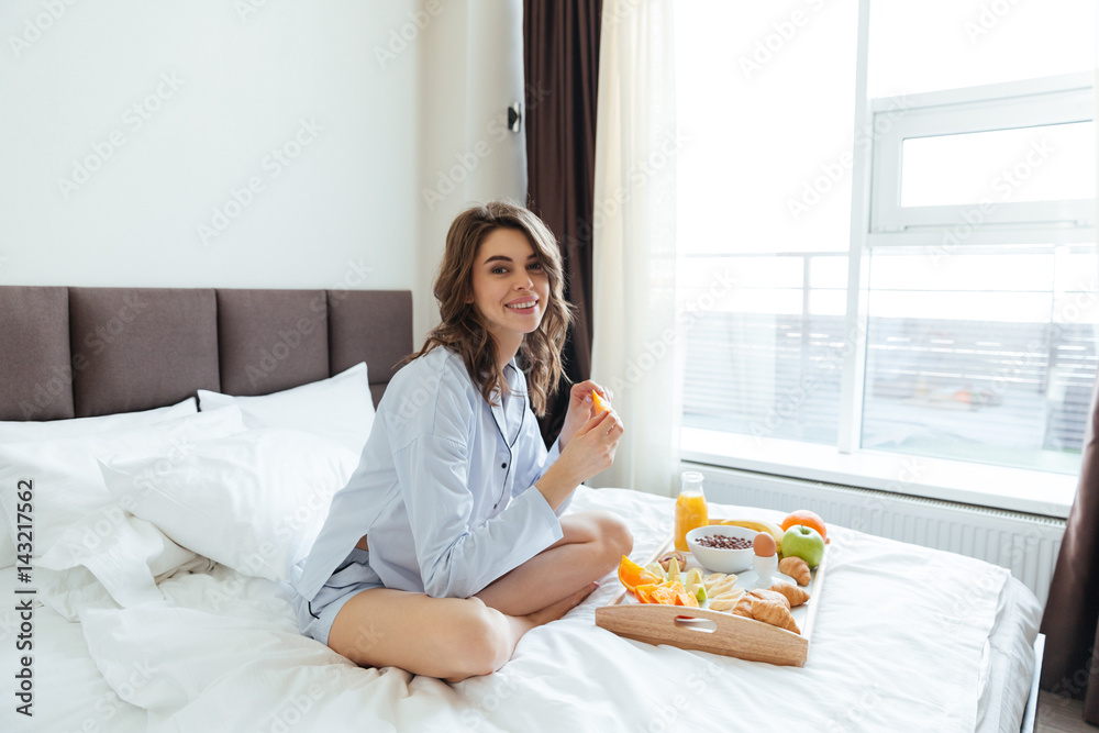 Portrait of a pretty happy woman having breakfast in bed