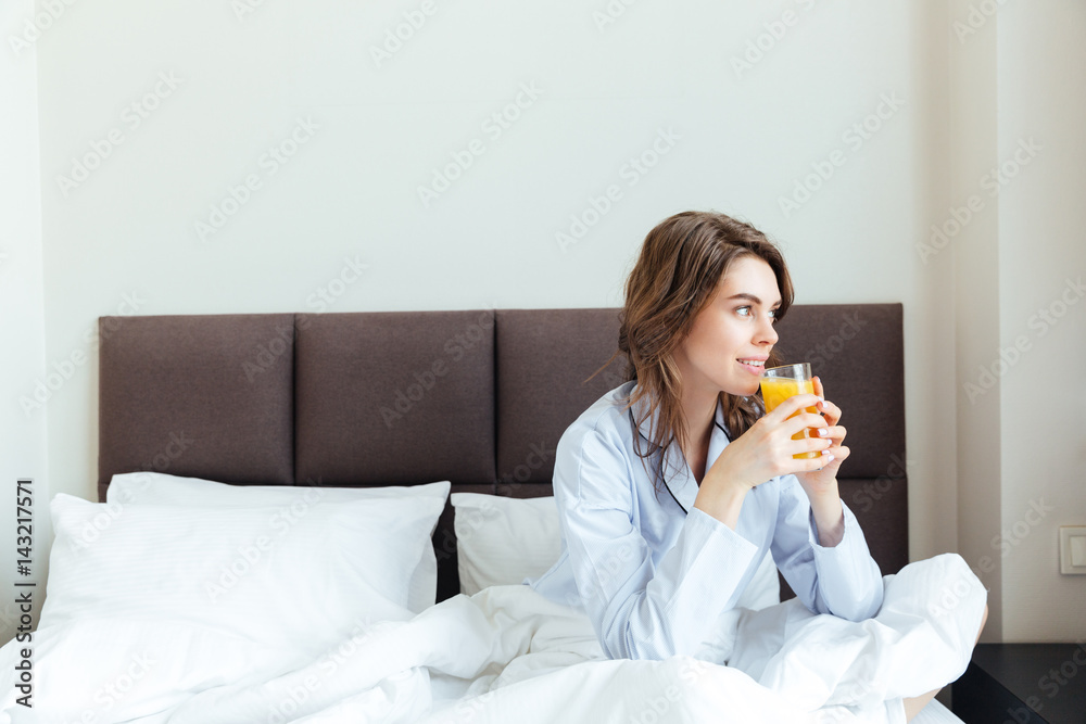 Portrait of a beautiful woman drinking orange juice in bedroom