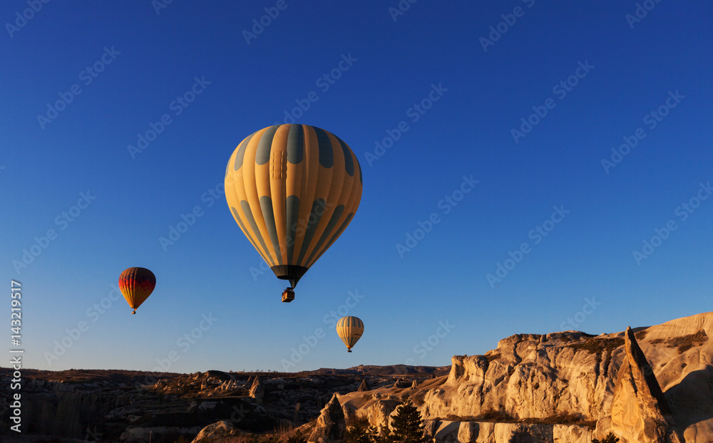 hot air balloon rises very high in blue sky above white clouds, bright sun shines