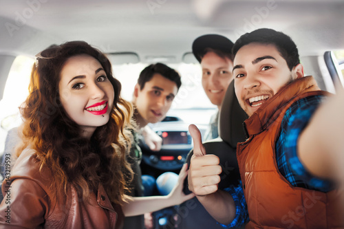 A company of four friends makes selfie inside the car