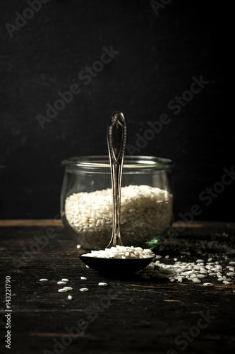 Raw Arborio rice on spoon and in jar on black background photo