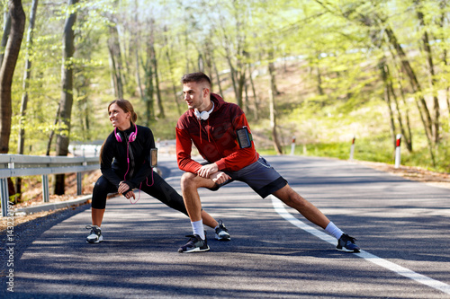 Young man and woman stretching muscles on the road before running. Young couple warming up.