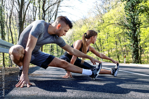 Young man and woman stretching muscles on the road before running. Young couple warming up.