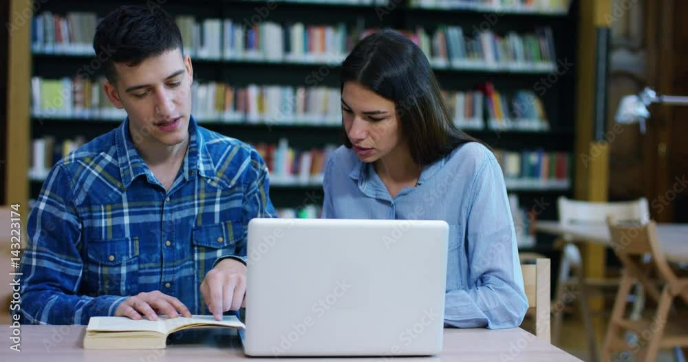 A couple of students, study and do research together on the library computer. Concept: teamwork, study, research, design. A couple of students, study and do research together on the library computer. Concept: teamwork, study, research, design.