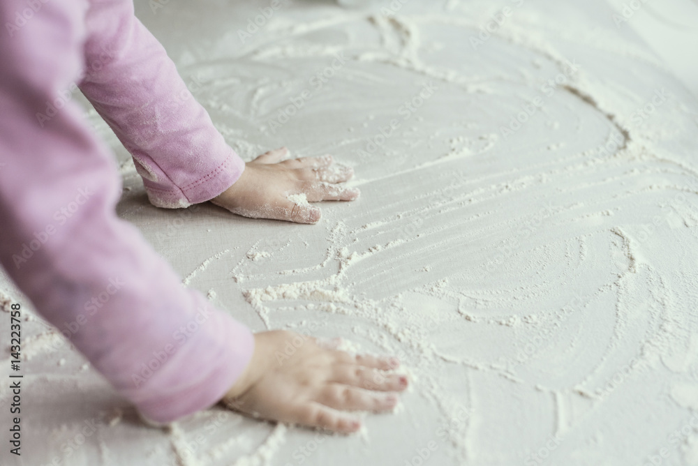 The little girl is playing in the kitchen, hands in flour