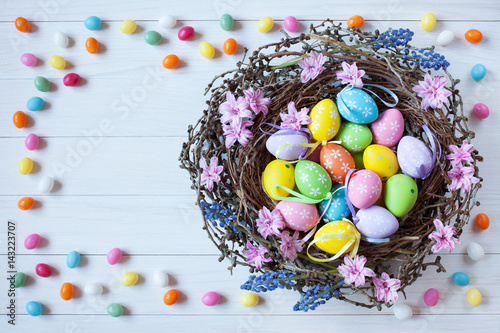 Easter nest with eggs and flowers on a light wooden background, candy