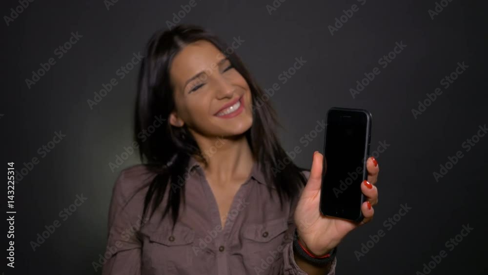 Young attractive woman holding smart phone in hand and pointing at it Young attractive woman holding smart phone in hand and pointing at it