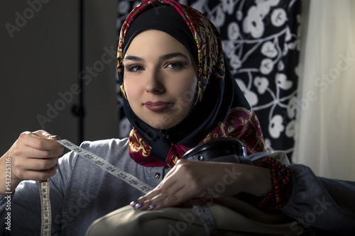 Female fashion designer tailoring conservative clothing in a textile workshop.  The hijab she is wearing is associated with muslims, middle east or eastern european cultures.  