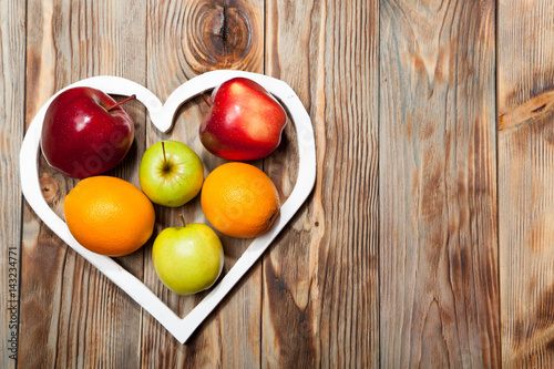 White heart, apples and oranges on the wooden background