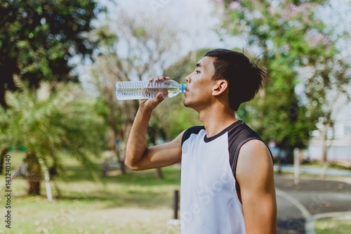 Sports man drinking water after exercising on background of green trees.