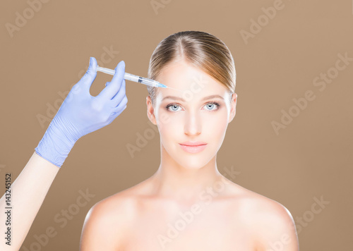 Young and beautiful woman having skin injections over brown background. Plastic surgery concept.