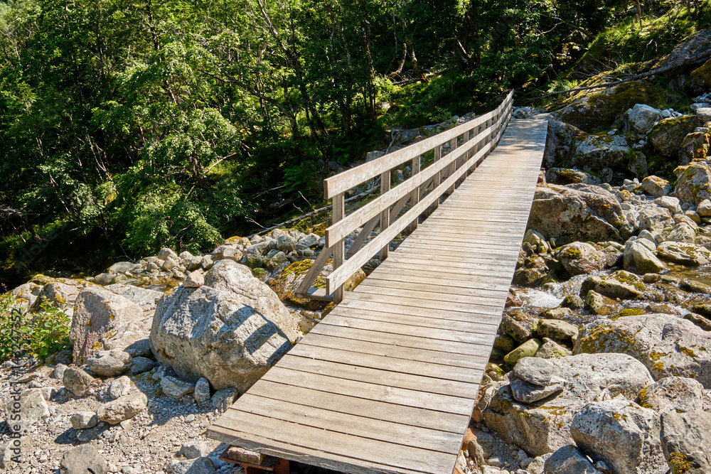 Simple narrow bridge made of planks leading over a river running between granite boulders near lake Bondhus in Norway