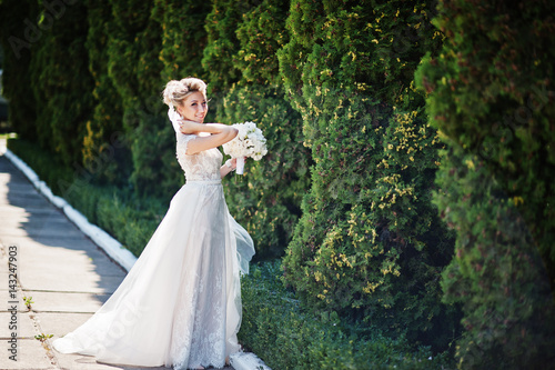 Awesome gorgeous blonde bride with wedding bouquet at hands at sunny day.