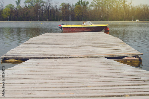 Wooden Pier In A Sunny Day With Parked Boat In Front Of It With Sunlight Behind