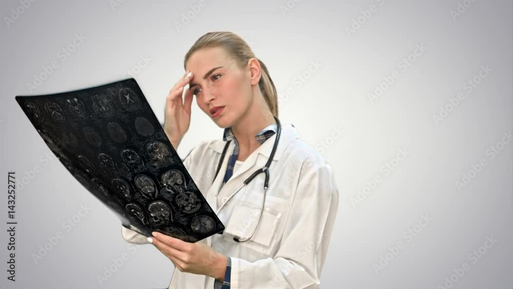Female doctor looking seriously at xray results of human brain on white background. Female doctor looking seriously at xray results of human brain on white background.