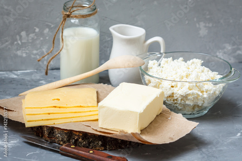 Various dairy products: Cottage cheese, bottle of milk, butter and cheese pieces on a dark background
