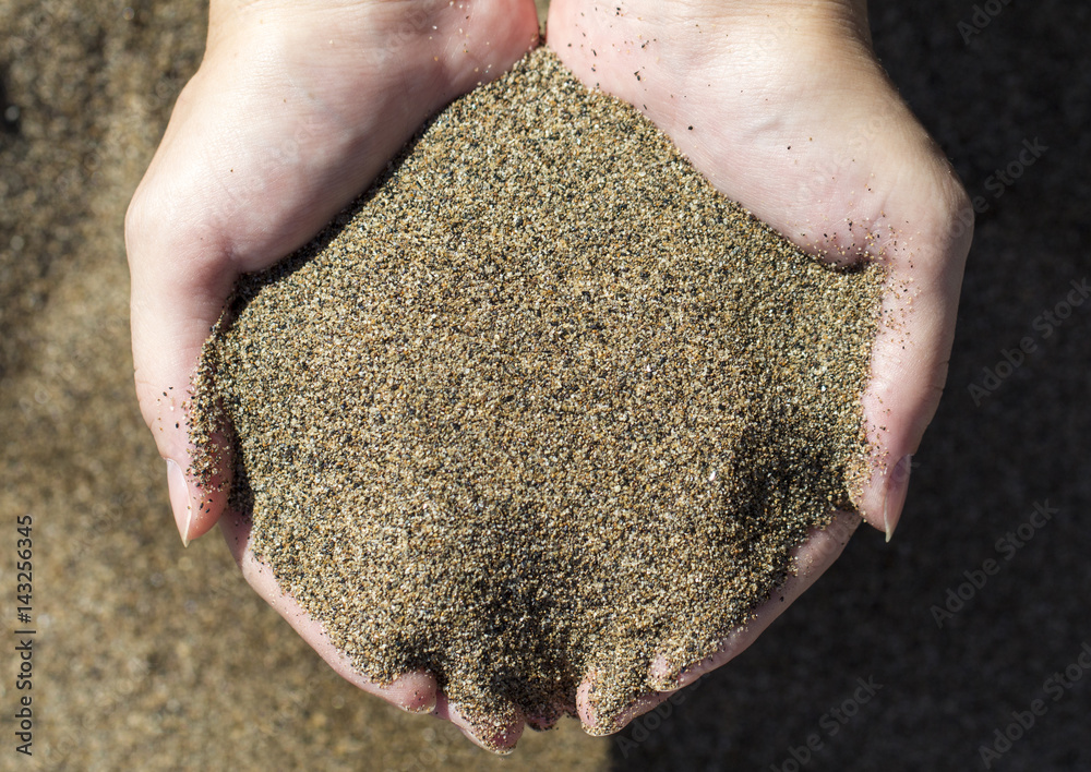 Two hands hold volcanic sand. Sand beach in hands top view photo.