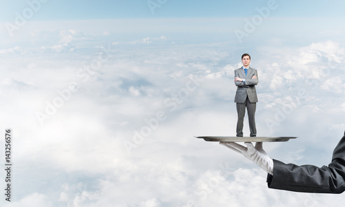 Confident businessman presented on metal tray against blue sky background © adam121