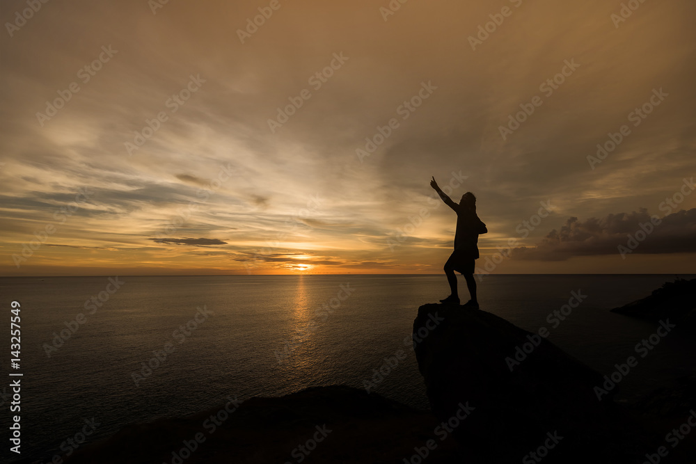 silhouette of man stand and hand up on rock in sunset.