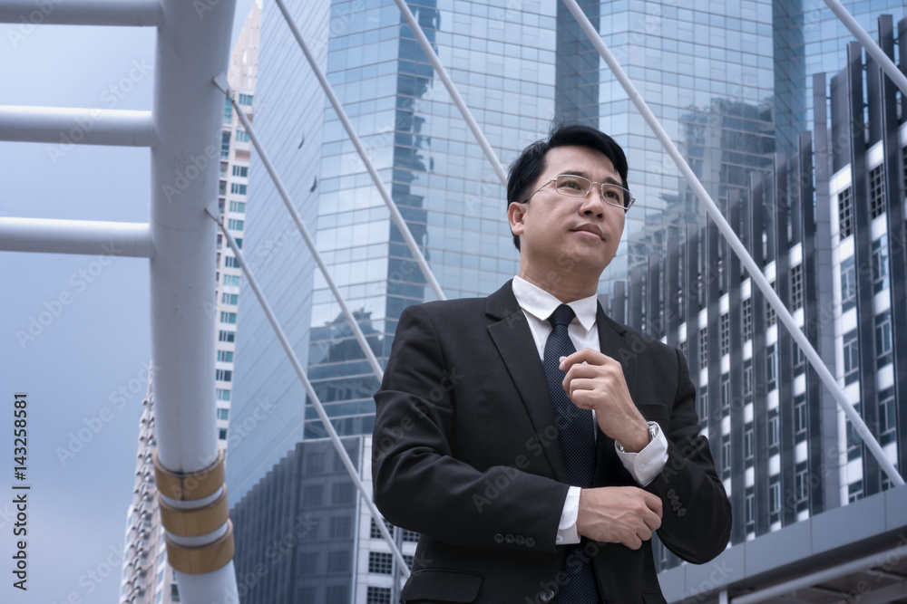 Asian confident Businessman standing in suit and looking away with modern city background Asian confident Businessman standing in suit and looking away with modern city background