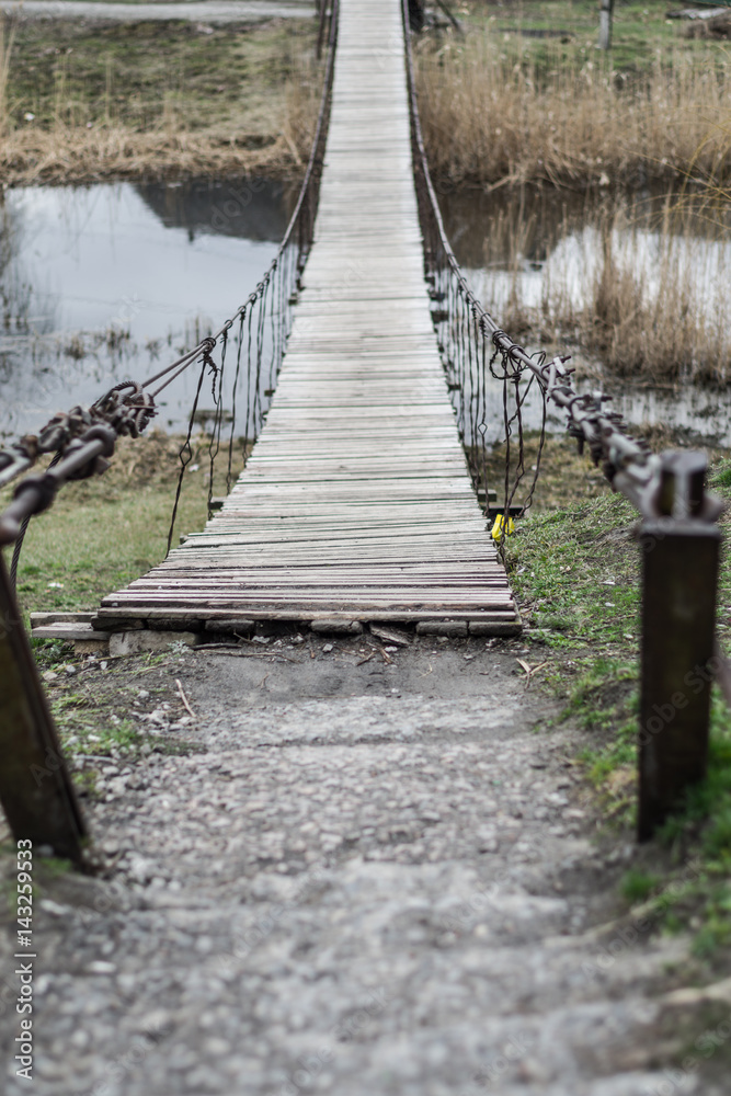 Old wooden hanging bridge with metal cables across the river. Old wooden hanging bridge with metal cables across the river.