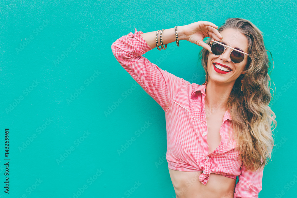 Colorful portrait of happy young  woman holding sunglasses. Green background.