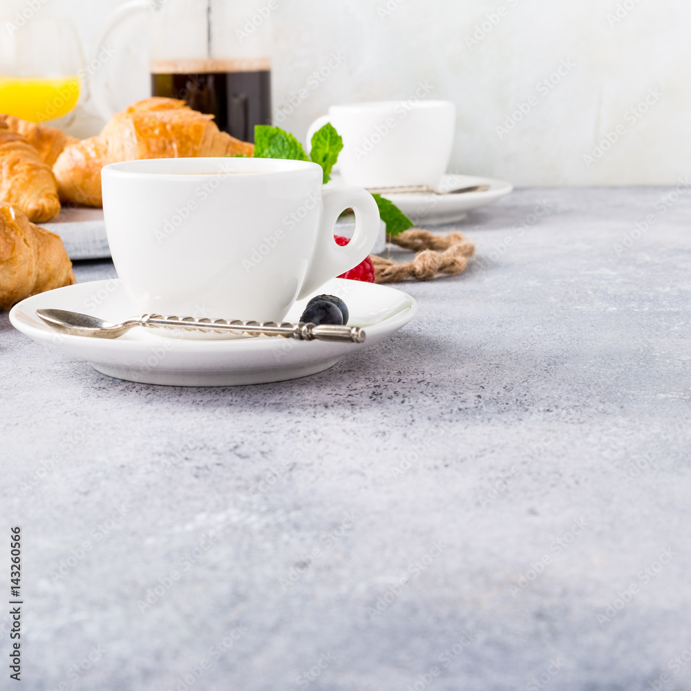 White cups of coffee and croissants on light gray background, selective focus. Healthy breakfast concept with copy space. White cups of coffee and croissants on light gray background, selective focus. Healthy breakfast concept with copy space.