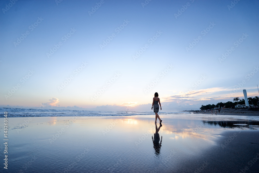 Fototapeta premium Niebo i morze. Piękny zachód słońca. Sylwetka młodej kobiety spaceru na plaży oceanu.