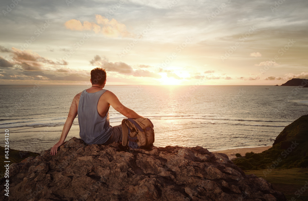 Traveller with backpack enjoying sunset on mountain.