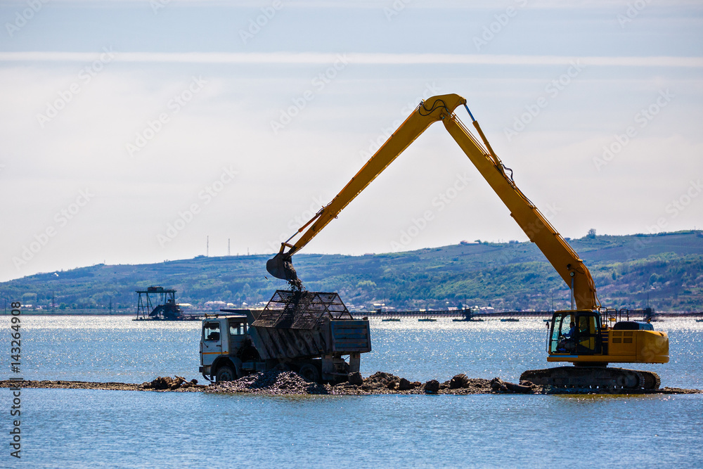 an excavator loads a dump sand in the water an excavator loads a dump sand in the water