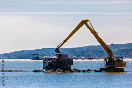 an excavator loads a dump sand in the water © czamfir