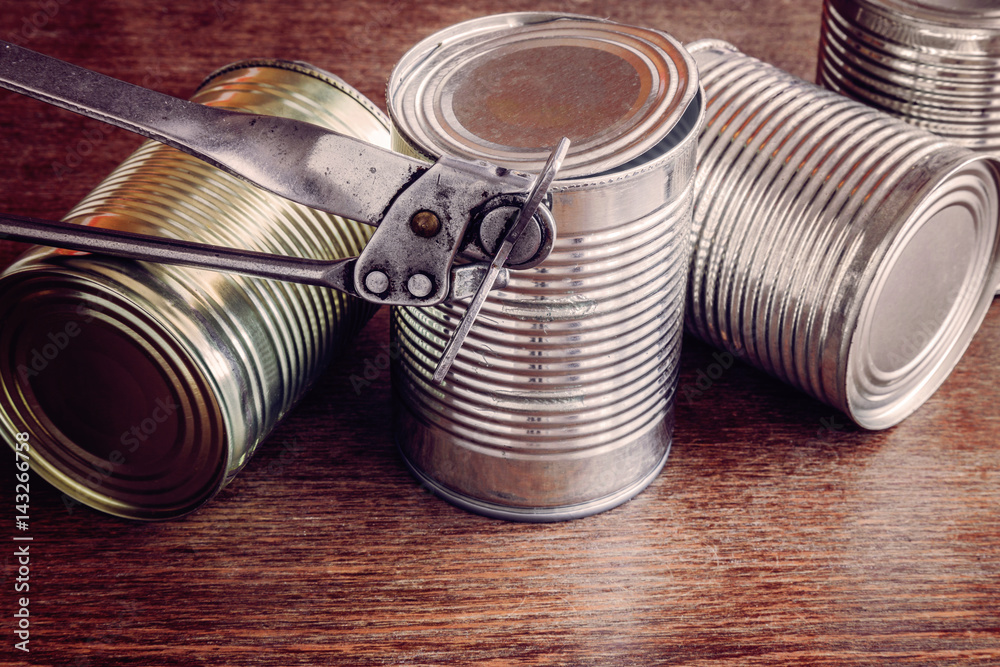 Old opener open to metallic can on the table in the kitchen. Canned