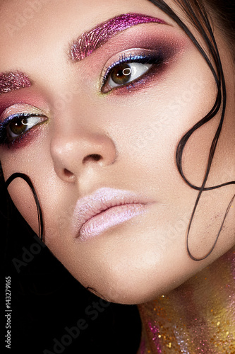 Young girl with creative makeup and shiny eyebrows. Beautiful model with strands of hair on face and perfect skin. Beauty of the face. Photo taken in studio. Shining neck, covered with sequins. Macro