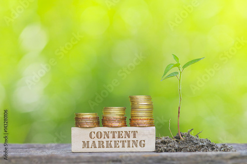 CONTENT MARKETING Golden coin stacked with wooden bar on shallow DOF green background.