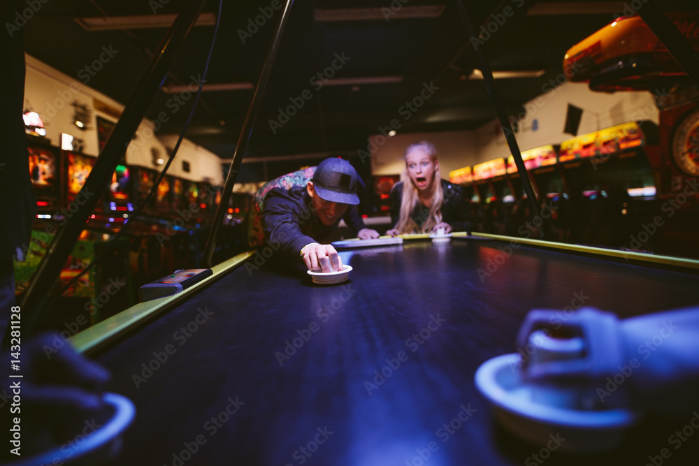 Happy young friends playing air hockey at amusement park