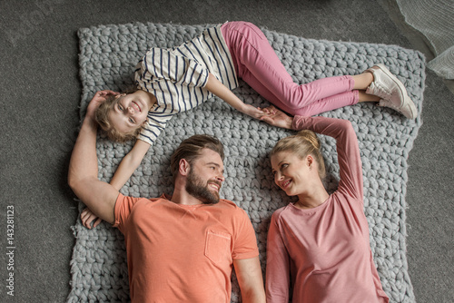 Top view of happy family with one child lying together on grey knitted carpet