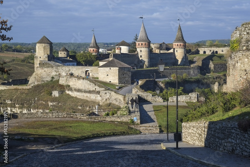 View of the Most Zamkowy and Castle of Kamianets-Podilskyi in Western Ukraine taken on a sunny autumn day. The cobbled street leads the eye across the bridge to the castle