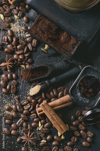 Black roasted coffee beans and grind with spices cinnamon, anise, cardamom, clove and brown sugar. With black vintage coffee grinder and scoops over wood burnt background. Top view