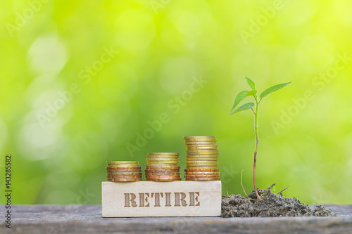 RETIRE WORD Golden coin stacked with wooden bar on shallow DOF green background.