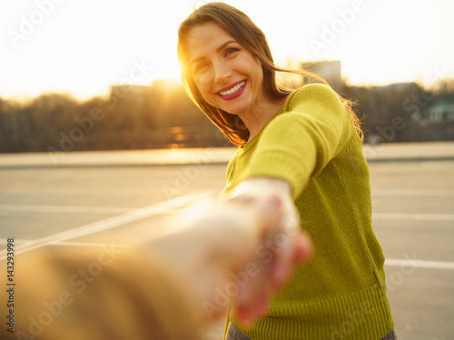 Follow me - happy young woman pulling guy's hand - hand in hand walking on a bright sunny day