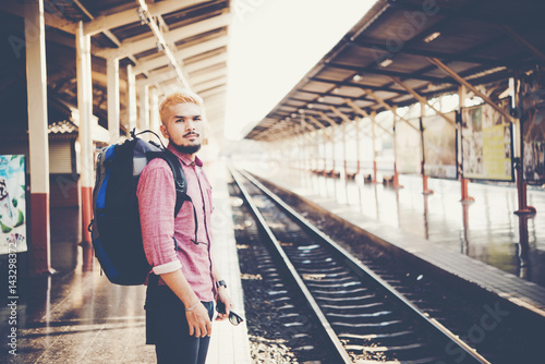 Young tourist man with backpack standing on platform waiting for train at train station, vintage tone filter effects.Travel concept. © MollyP