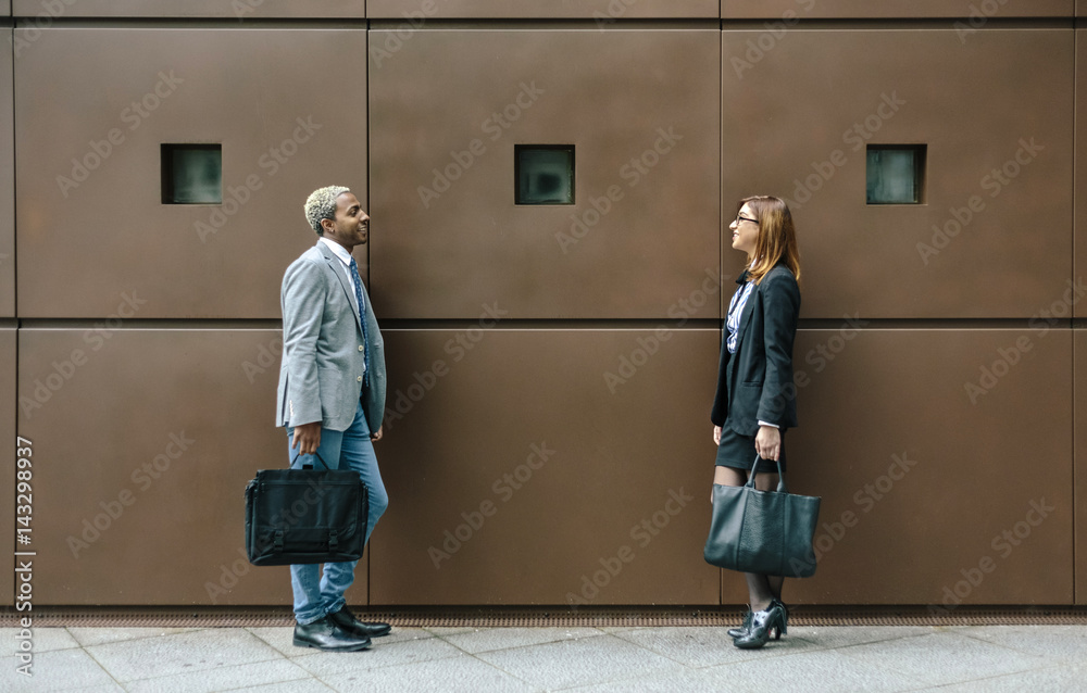 Young businessman and woman standing in front of steel wall, talking