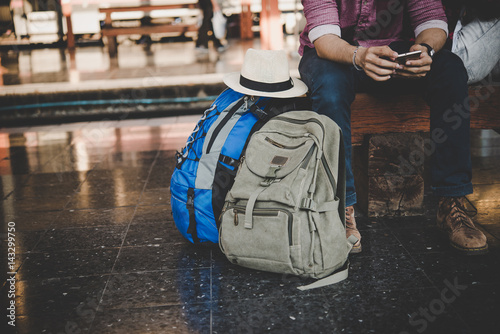 Close up of Young hipster traveller man siting on bench with backpack in train station waiting for go travel with the train. Travel concept.