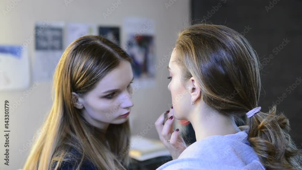 Make-up artist doing makeup for model before photo session. Visagiste with long blond hair holds professional shades brush for makeup lips in space studio. Woman with brown picked tail prepares for Make-up artist doing makeup for model before photo session. Visagiste with long blond hair holds professional shades brush for makeup lips in space studio. Woman with brown picked tail prepares for