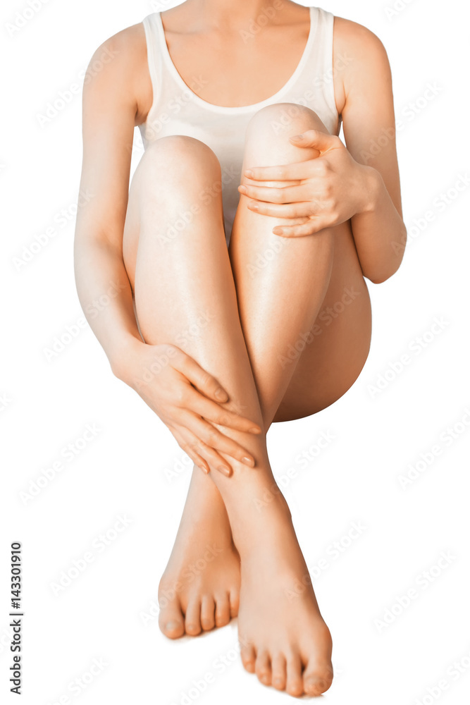 Beautiful barefoot woman sitting on the floor. Close up of slender naked legs being massaged isolated on white - healthcare and beauty concept