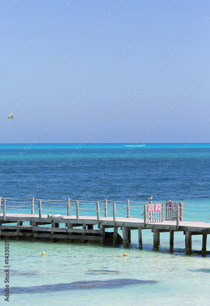 View to the sea. Turquoise water of the Caribbean sea. Wooden pier, long bridge. Parasailing in the background.