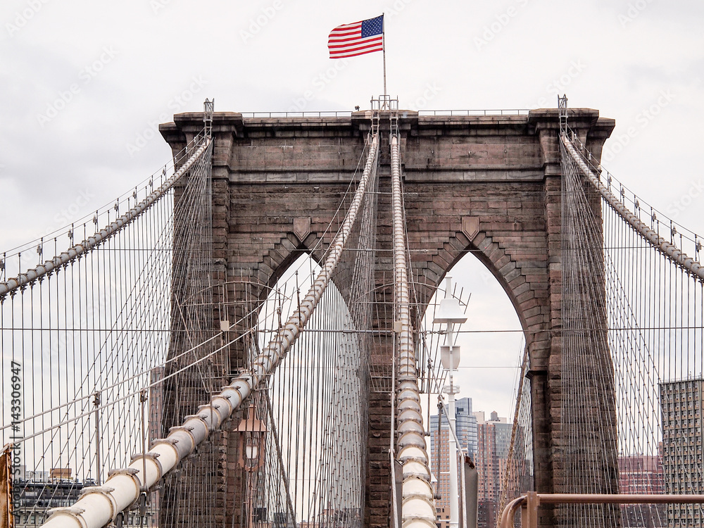 Obraz premium American flag waving on top of Brooklyn Bridge tower, New York City, NY, USA